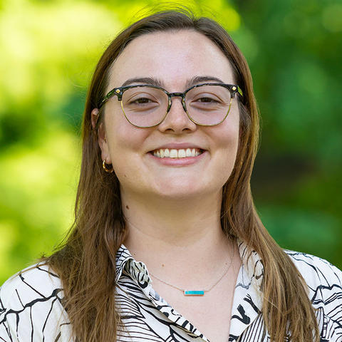 Headshot of Sophie Goodfellow, smiling for the camera against a soft focus background of Haverford College foliage